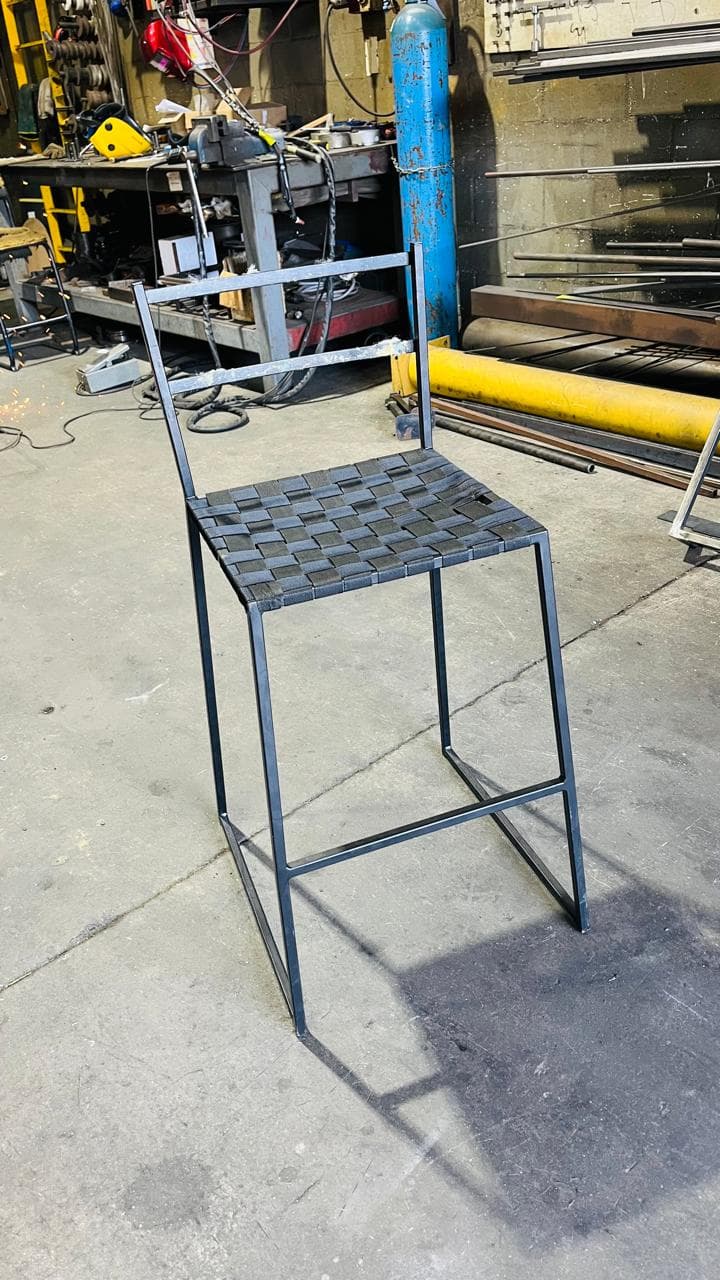 Custom metal chair with a woven metal seat and footrest in the workshop